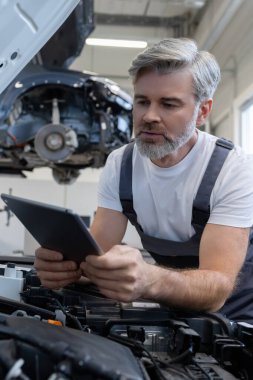 Tamirci otomobil tamirhanesinde motor kaputu açık tabletle teşhis koyuyor.
