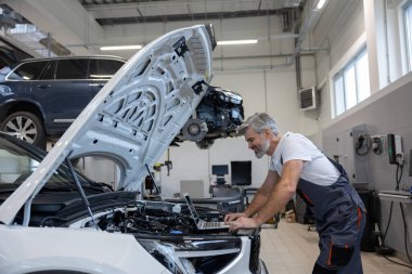 Oto tamir atölyesinde kaputu açık motor tanılama için dizüstü bilgisayar kullanan bir tamirci.
