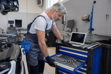 Tamirci, otomatik tamir atölyesinde dizüstü bilgisayarlı araç kutusundan araç seçiyor