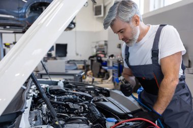 Oto tamir atölyesinde kaputu açık aracın yanında çalışan tamirci.
