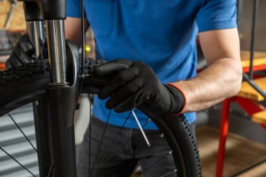 Tamircinin elleri atölyede tamir masasında bisiklet tekerleğini ayarlıyor.