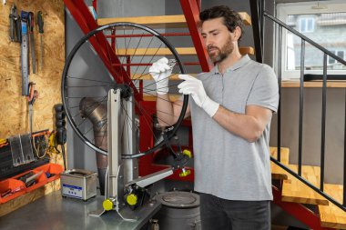 Beyaz eldivenli tamirci atölyede bisiklet çarkını inceliyor.