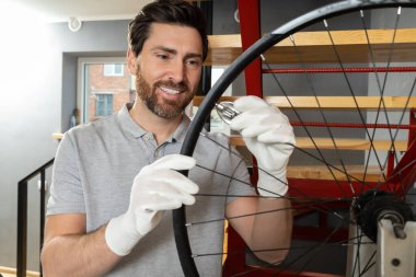 Beyaz eldivenli tamirci atölyede aletlerle bisiklet tekerleği tutuyor.