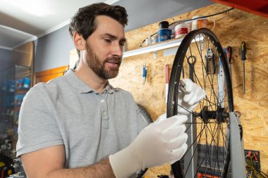 Beyaz eldivenli tamirci atölyede bisiklet tekerleği tutuyor.