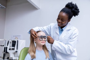 Optometriste. Afrikalı Amerikalı kadın optometrist küçük bir hastanın görüşünü kontrol ediyor.
