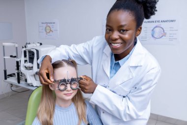 Optometriste. Afrikalı Amerikalı kadın optometrist küçük bir hastanın görüşünü kontrol ediyor.
