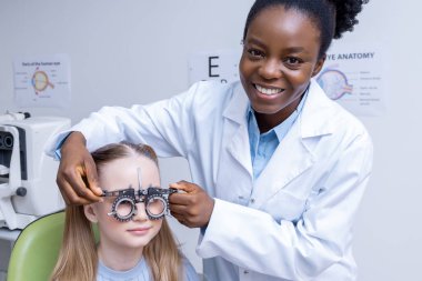 Optometriste. Afrikalı Amerikalı kadın optometrist küçük bir hastanın görüşünü kontrol ediyor.