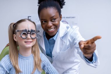 Optometriste. Afrikalı Amerikalı kadın optometrist küçük bir hastanın görüşünü kontrol ediyor.