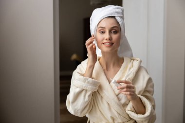 Kafasına havlu sarılmış, cildine krem süren sakin bir kadın.