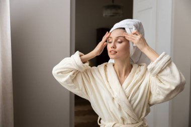 Beyaz bornozlu güzel bir kadın cildine doğal yüz temizleyici sürüyor. Sakinleştirici cilt bakımı rutini sırasında.