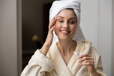 Beyaz bornozlu güzel bir kadın cildine doğal yüz temizleyici sürüyor. Sakinleştirici cilt bakımı rutini sırasında.