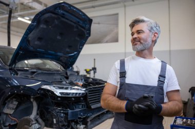 Kaputu açık aracın yanındaki tamircide eldivenli bir tamirci duruyor.