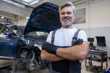 Kaputu açık aracın yanındaki tamircide eldivenli bir tamirci duruyor.