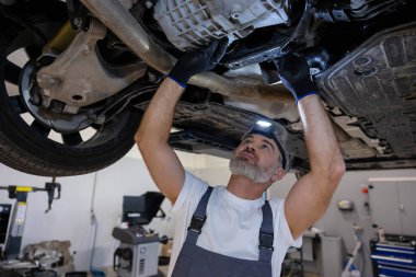 Tamirci, oto tamirhanesinde asansördeki şasiyi incelemek için farları kullanıyor.