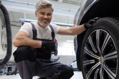 Aracın yanında çömelirken oto tamir atölyesinde mekanik inceleme çarkı