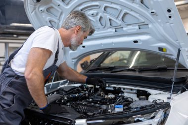 Oto tamirhanesinde kaputu açık motor dipstick ile yağ seviyesini kontrol eden tamirci.