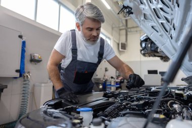 Oto tamirhanesinde kaputu açık motor dipstick ile yağ seviyesini kontrol eden tamirci.