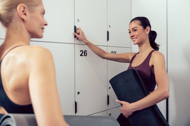 Sohbet. Spor salonunda soyunma odasında konuşan iki genç kadın.