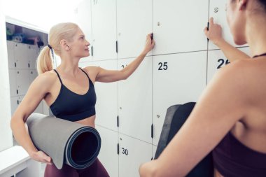 Sohbet. Spor salonunda soyunma odasında konuşan iki genç kadın.