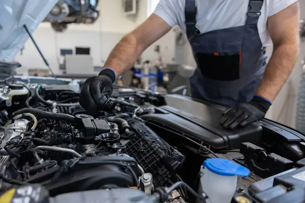 Oto tamirhanesinde kaputu açık motor dipstick ile yağ seviyesini kontrol eden tamirci.