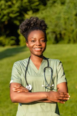 Parktaki hemşire. Parkta boynunda laboratuvar önlüğü ve steteskop olan Afrikalı Amerikalı genç bir kadın.