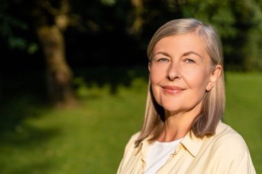 İyi hissediyorum. Kafkasyalı olgun, gülümseyen bir kadın ayakta mutlu bir bakışla duruyor.