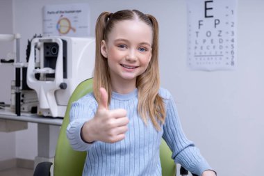 Doktoru ziyaret et. Gülümseyen tatlı kız göz doktorunun ofisinde oturuyor ve mutlu görünüyor.