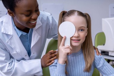 Vizyon testi. Afrikalı Amerikalı optometrist küçük bir hastayla çalışıyor ve dost canlısı görünüyor.