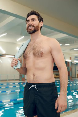 Havuzda. Omzunda havluyla havuzda duran beyaz sakallı genç adam.