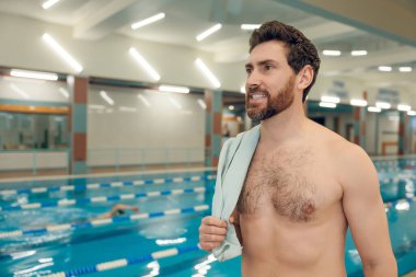 Havuzda. Omzunda havluyla havuzda duran beyaz sakallı genç adam.