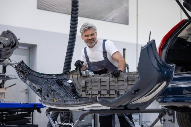 Tamircinin arka tamponu oto tamirhanesinde açık bagajın yanında duruyor.