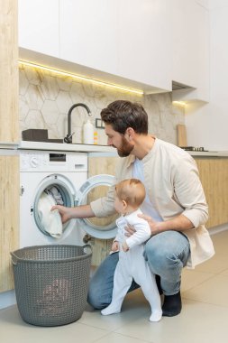 Ev işi. Genç adam ve küçük oğlu çamaşır makinesine koymadan önce elbiselerini ayırıyorlar.