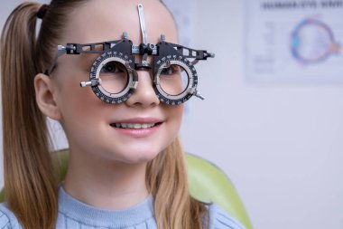Optometri. Açık renk saçlı okul kızı klinikte optometri testi yaptırıyor.