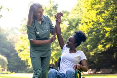 Rehabilitasyon. Parkta Afrikalı Amerikalı bir kadın hastayla rehabilitasyon egzersizleri yapan hemşire.