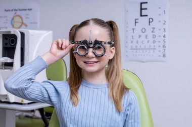 Optometri. Açık renk saçlı okul kızı klinikte optometri testi yaptırıyor.