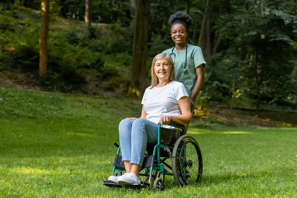 Güzel yürüyüş. Tekerlekli sandalyedeki kadın, parkta bir hemşireyle yürürken mutlu görünüyor.