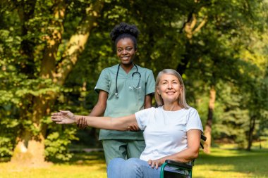 Güzel yürüyüş. Tekerlekli sandalyedeki kadın, parkta bir hemşireyle yürürken mutlu görünüyor.