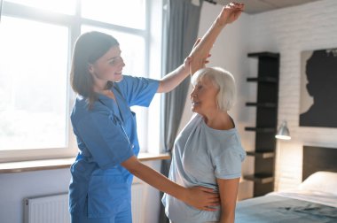 Egzersiz yapıyorum. Yaşlı bayan bir eğitmenle egzersiz yapıyor ve ilgili görünüyor.