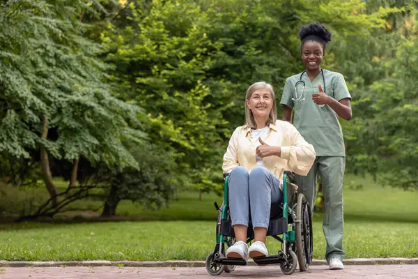 Keyfin yerinde. Tekerlekli sandalyedeki kadın parkta bir hemşireyle yürürken kendini harika hissediyor.