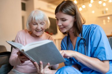 Birlikte okuyoruz. Yaşlı bir bayana kitap okuyan bir kadın bakıcı.