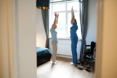 Egzersiz yapıyorum. Yaşlı bayan bir eğitmenle egzersiz yapıyor ve ilgili görünüyor.