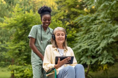 Sabah yürüyüşü. Tekerlekli sandalyedeki kadın ve hemşire parkta yürüyor.