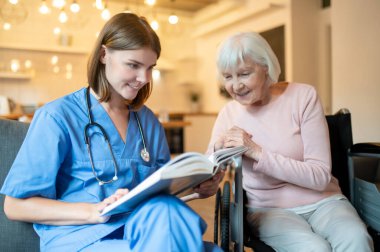 Birlikte okuyoruz. Yaşlı bir bayana kitap okuyan bir kadın bakıcı.