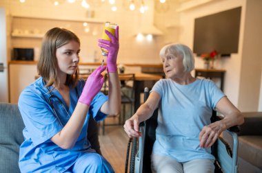 İğnelerin kutsallığı. Üniformalı hemşire iğneye ilaç hazırlıyor, yaşlı hasta korkmuş görünüyor.