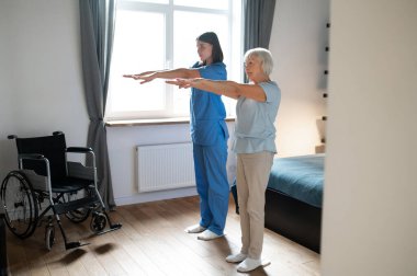 Egzersiz yapıyorum. Yaşlı bayan bir eğitmenle egzersiz yapıyor ve ilgili görünüyor.