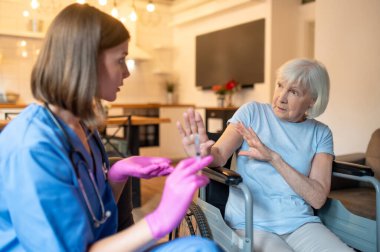 İğnelerin kutsallığı. Üniformalı hemşire iğneye ilaç hazırlıyor, yaşlı hasta korkmuş görünüyor.