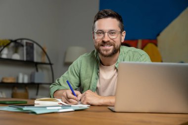 İç işlerinde bilgisayar ve kağıtlarla çalışırken masadaki notları inceleyen sakallı adam.