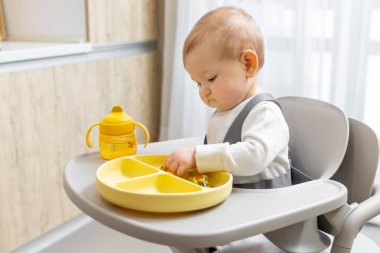 Bebek yemek yiyor. Sandalyesinde oturan ve sarı tabağından yemek yiyen tatlı bir çocuk.