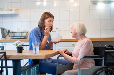 Kahvaltıda. Bakım asistanı yaşlı bayanı besliyor ve ikisi de memnun görünüyor.