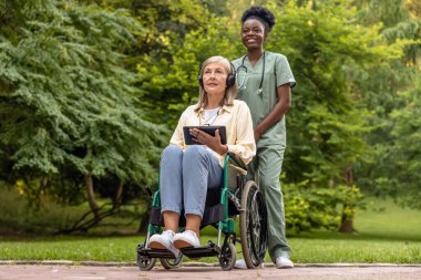Sabah yürüyüşü. Tekerlekli sandalyedeki kadın ve hemşire parkta yürüyor.